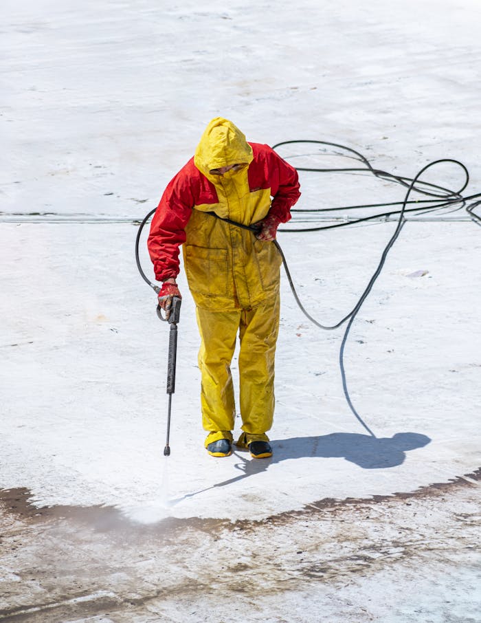 hero-img-02 Person in yellow and red safety suit cleaning with a pressure washer outdoors.